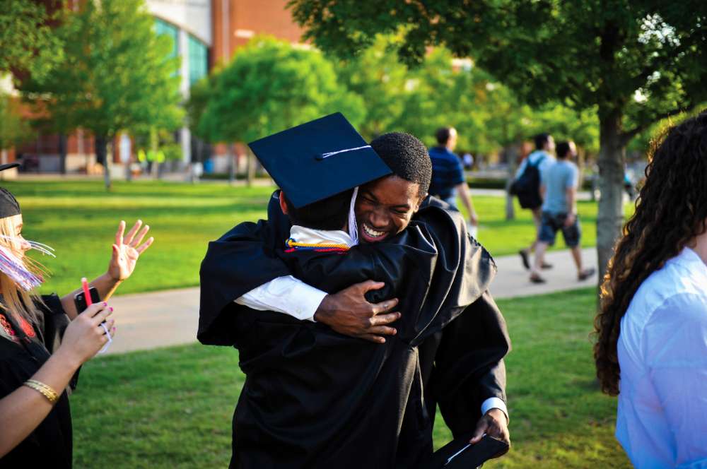 University of Oklahoma graduates in cap and gown hugging in celebration