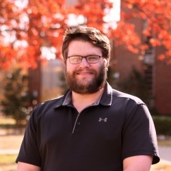 Eli Rhoades, black polo, on the South Oval, with fall leaves in the background