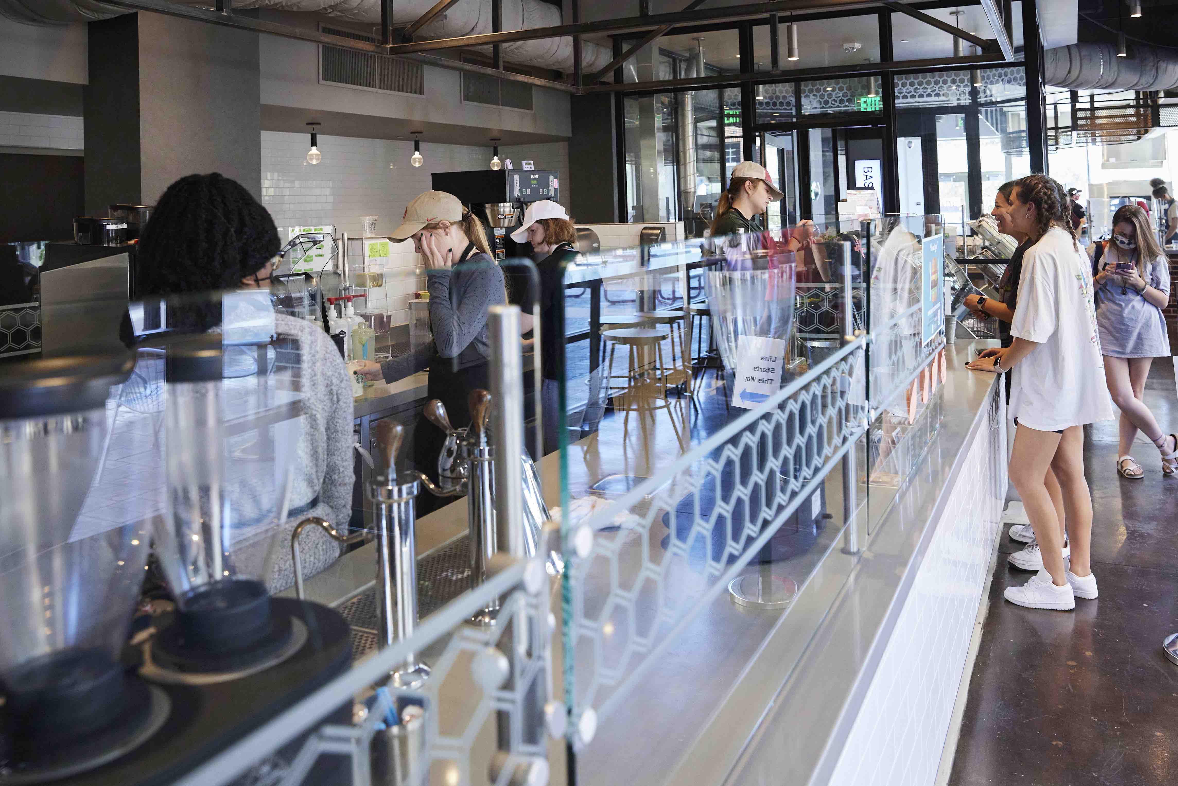 Several students stand in line to get food as employees prep items behind a counter.