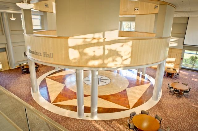 A photo of Founders Hall, a large windowed space with silver columns and a brown and rattan floor