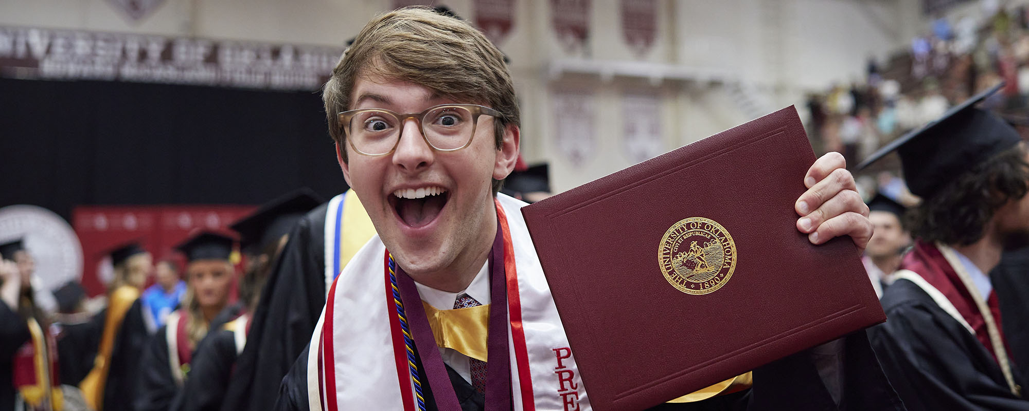 Student holding diploma cover and smiling during graduation ceremony.