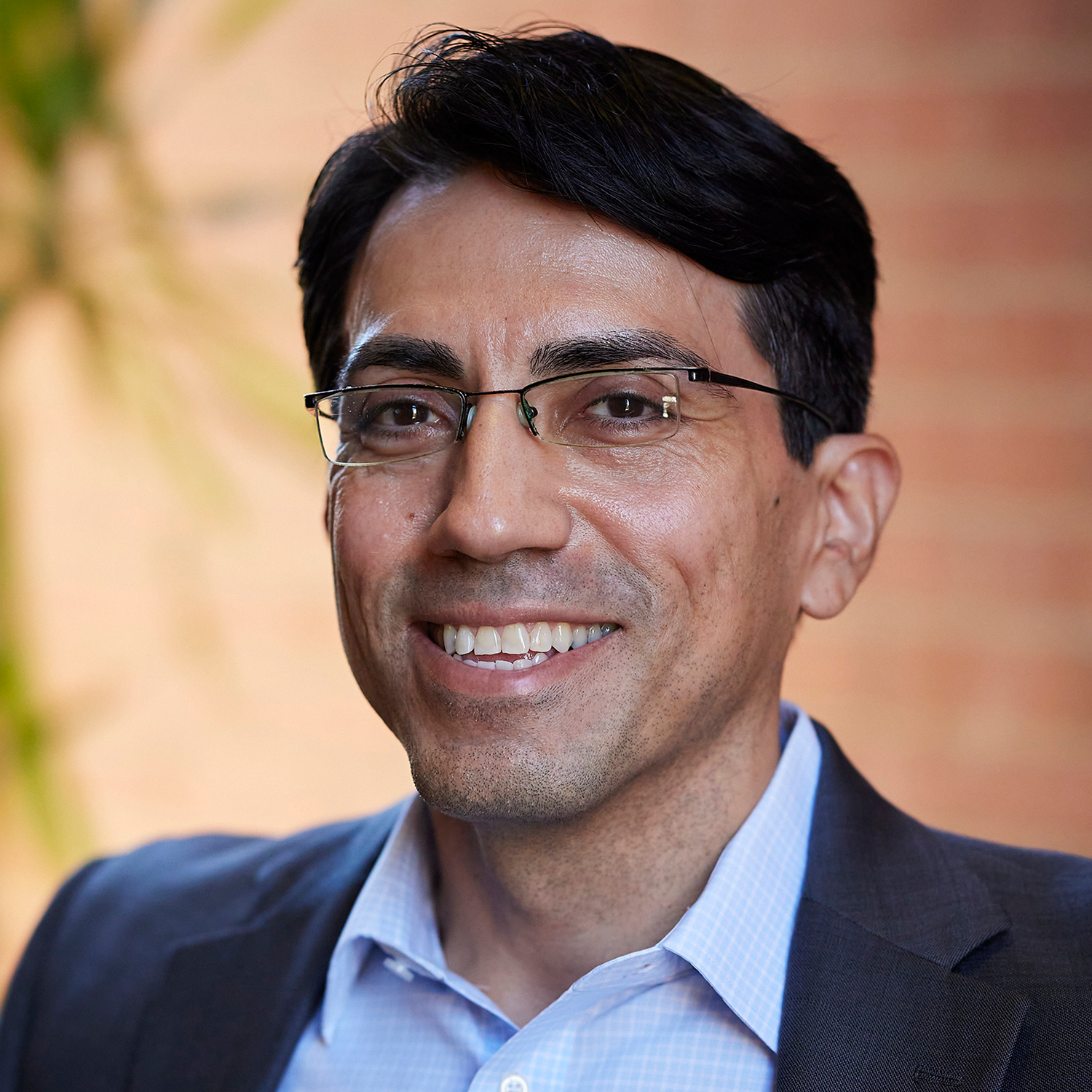 dark-haired man in blue oxford shirt with navy blazer wearing glasses 