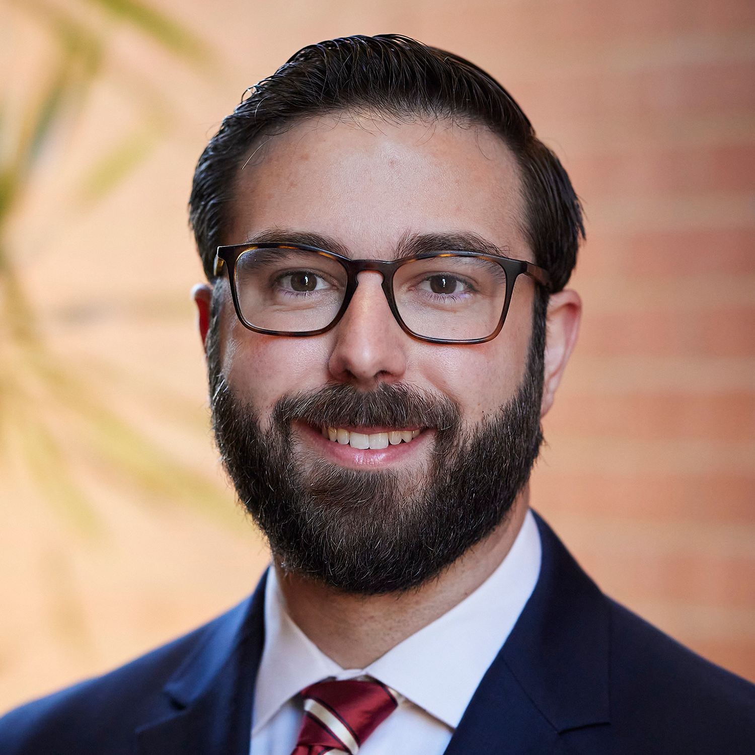 man in navy blazer with dark hair, beard and glasses