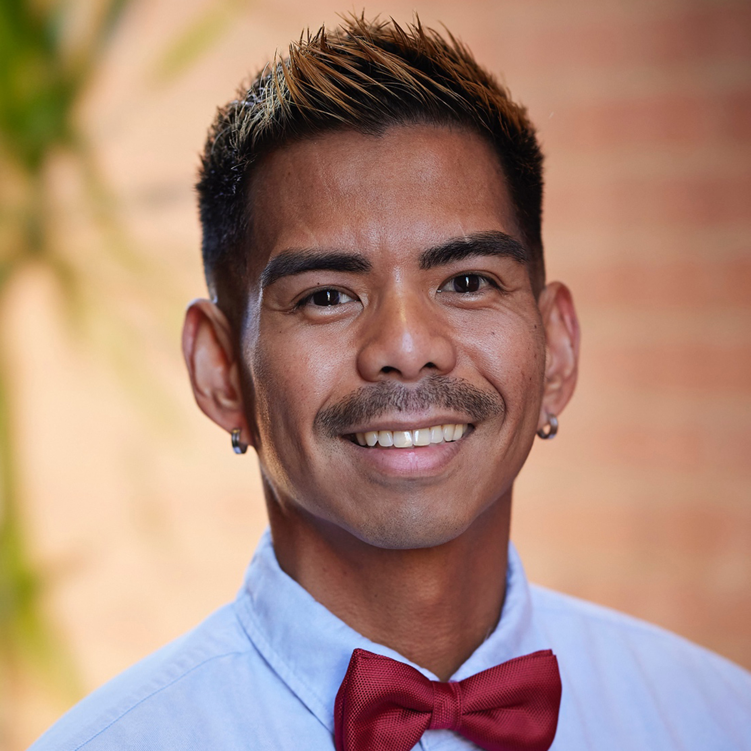 man in blue shirt with red bow tie and dark hair smiling