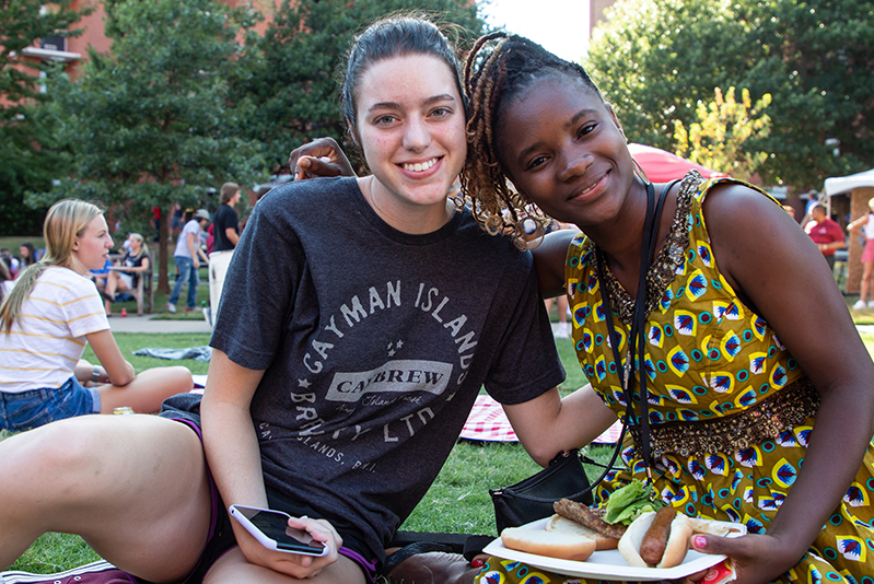 two OU students sitting on the lawn eating hot dogs