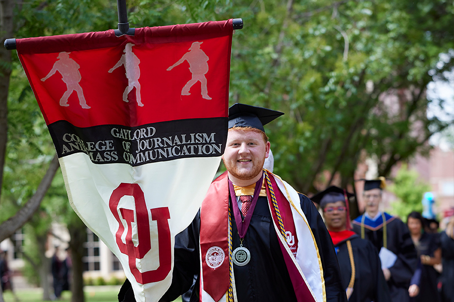 Jackson Conner walking in Gaylord College banner at May 2023 Convocation ceremony.