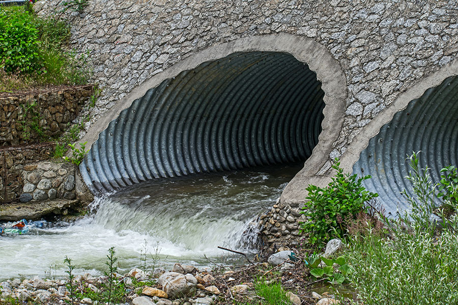 Water drains through pipes, under a bridge.