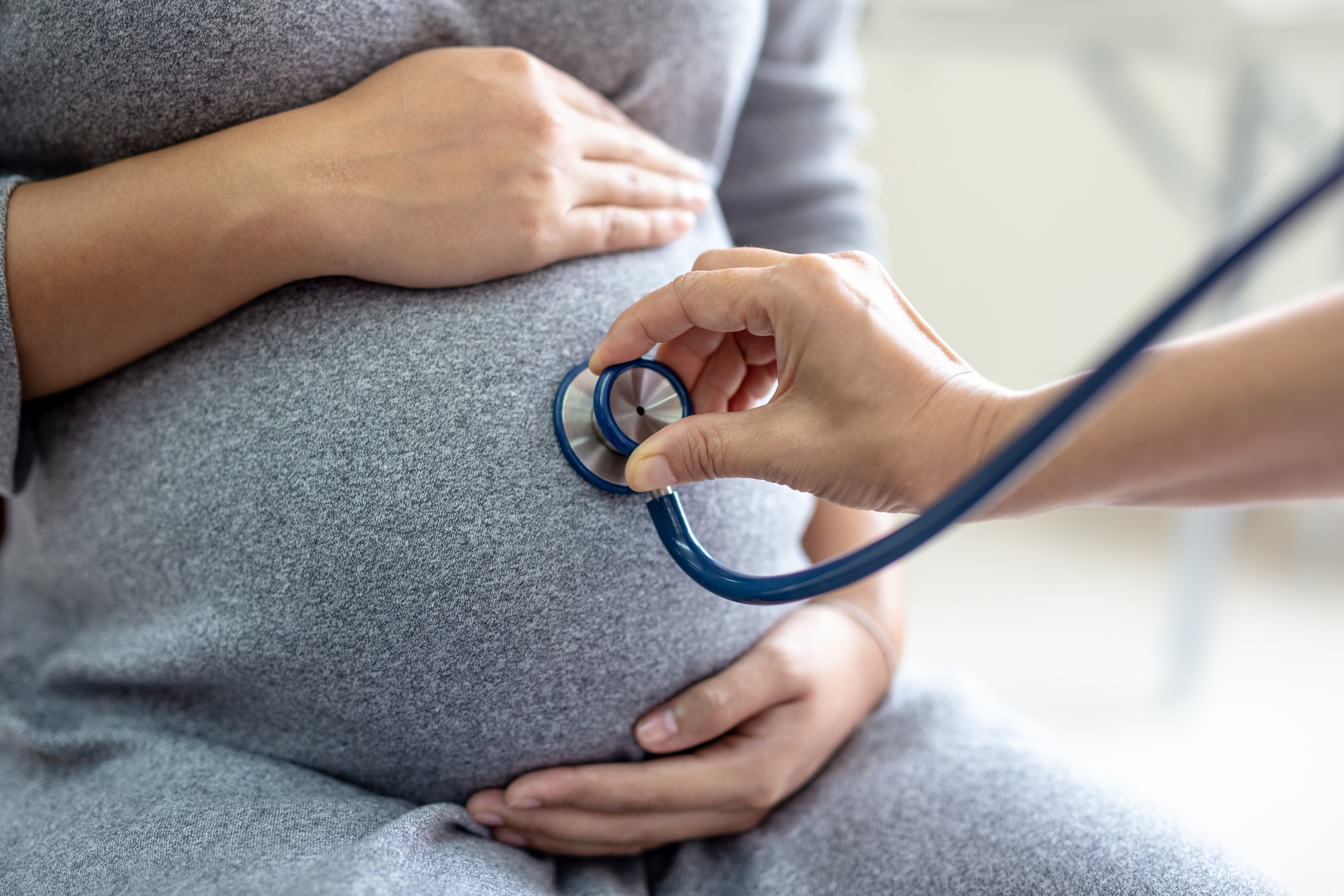 A pregnant woman holding her stomach as a doctor presses a stethoscope to it. 