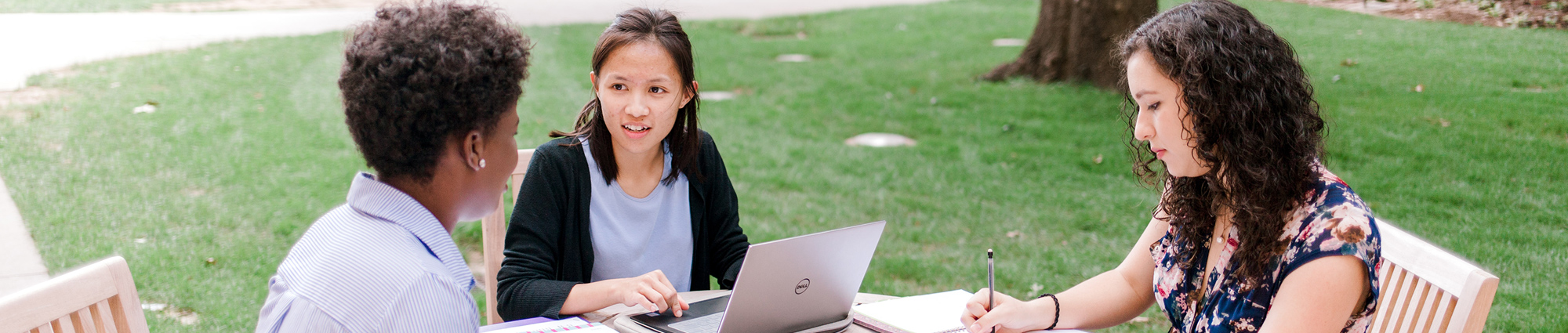 Three students work together on laptops in Dodson Courtyard in front of Price Hall