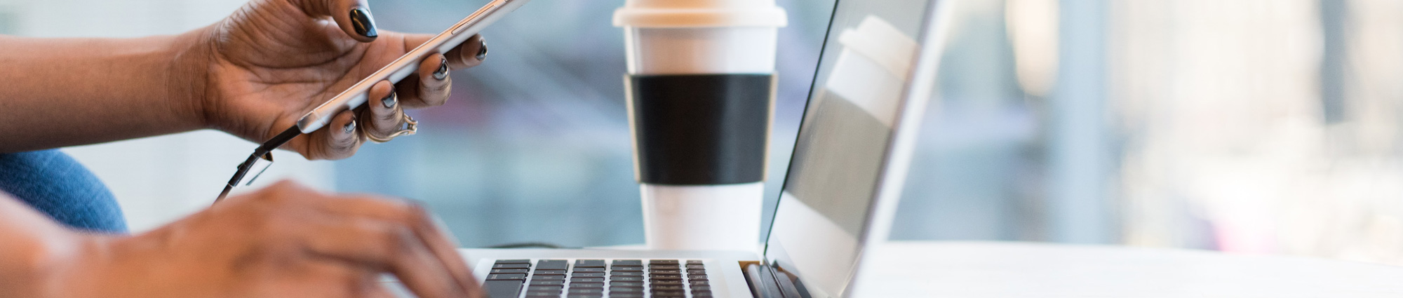 close up of a pair of hands, one typing on a laptop, while the other holds a cell phone