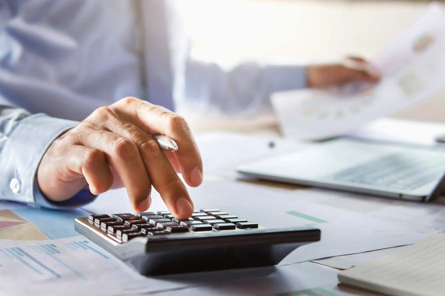 A person sitting at a desk holding a document in one hand and typing on a calculator with the other.