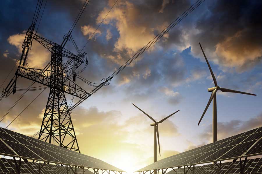 Solar panels, wind turbines and electrical power lines silhouetted against a sky at sunset. 