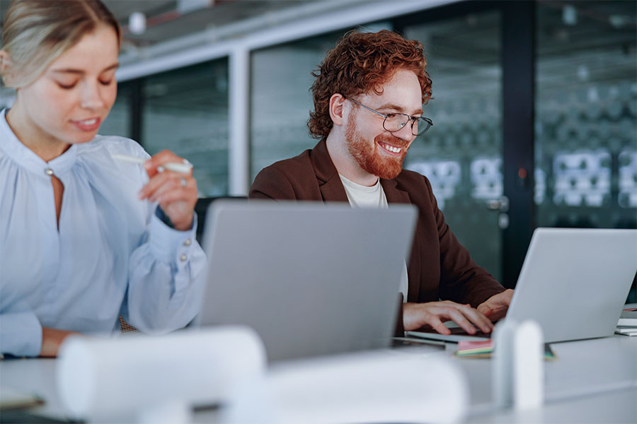 A professionally dressed man and woman working on laptops side-by-side.