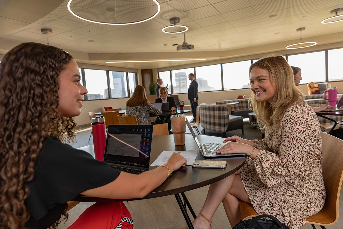 Two graduate school students work together in a study area on laptop computers.