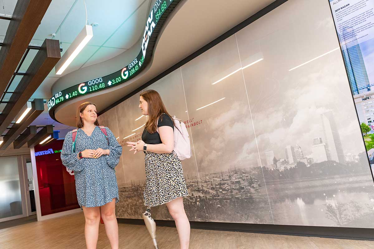 Two students engaged in a conversation in the hallway of the Gene Rainbolt Graduate School.