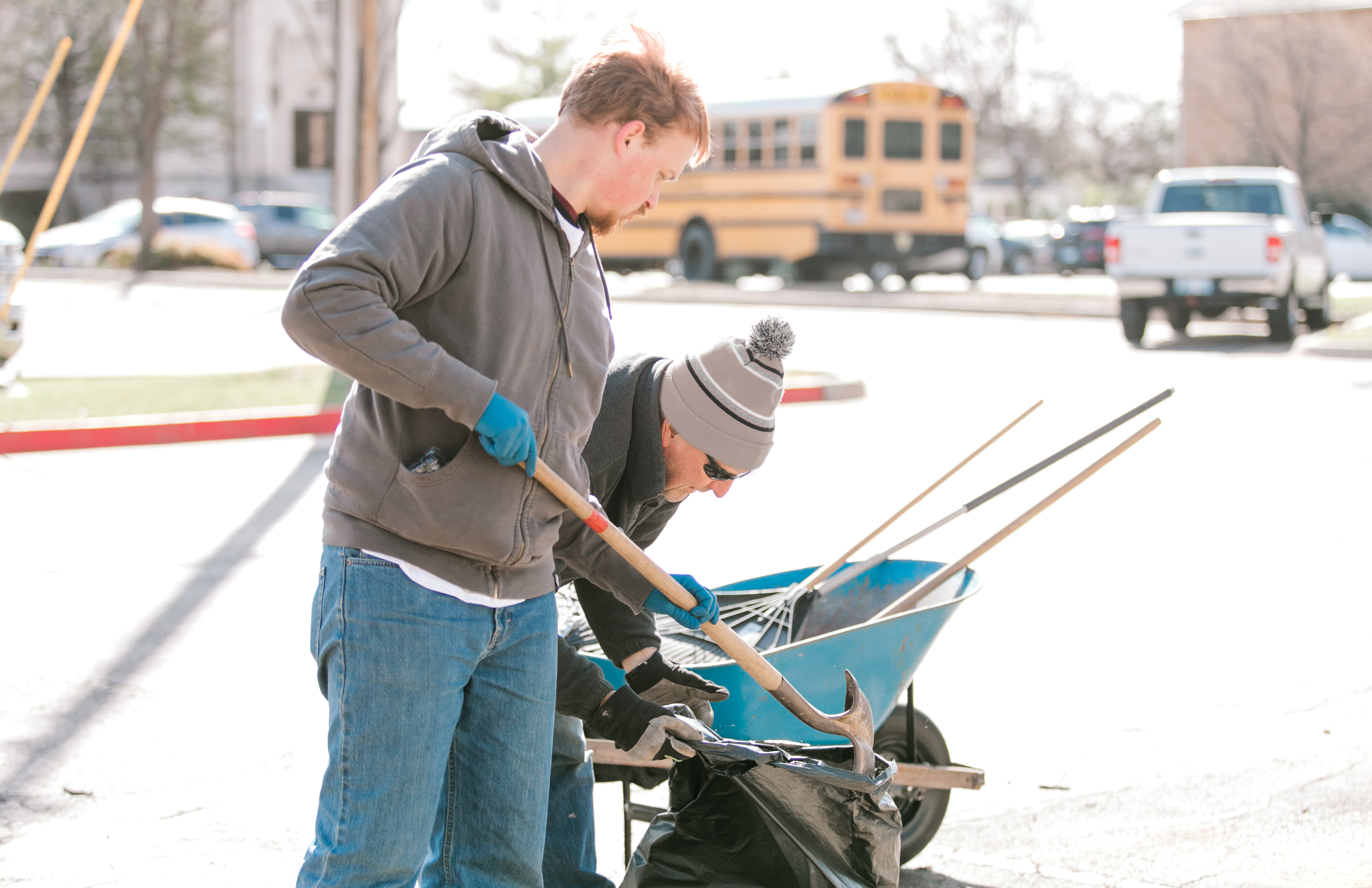 Two students volunteering using a shovel and a wheelbarrow. 