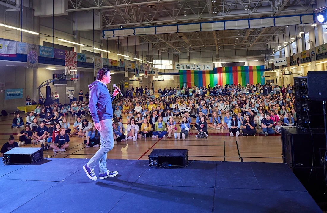 emcee standing on stage speaking to large group of students