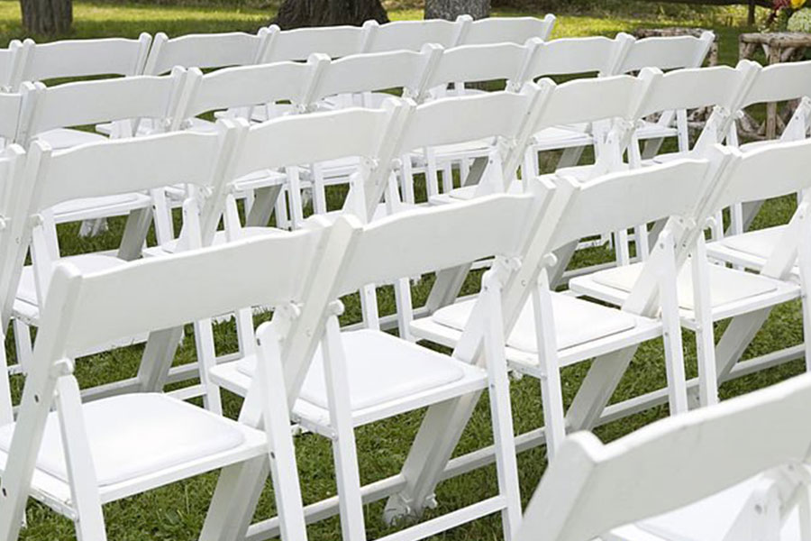 Lines of white folding chairs on grass.