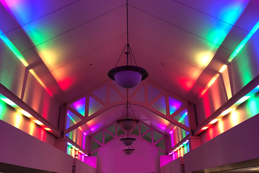 Multi-colored lighting shining up walls in large open-space room.