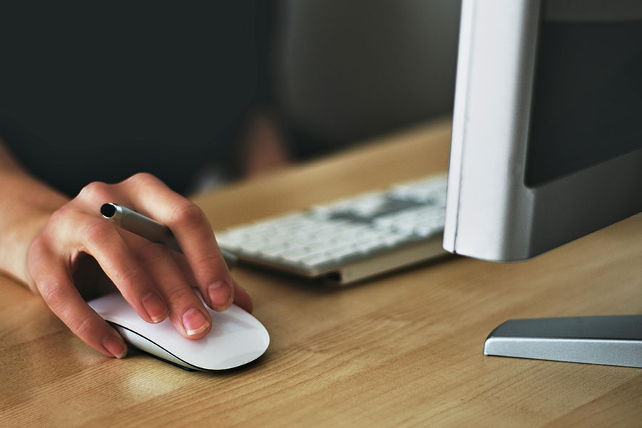 The person's hand on a wirelses computer mouse next to a keyboard.