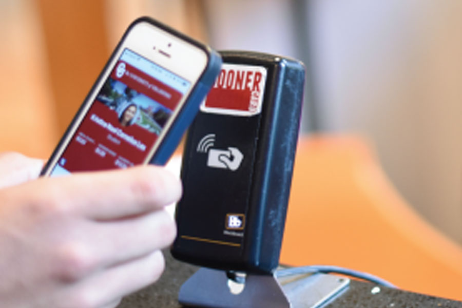 The mobile Sooner Card on a phone next to a card reader with Sooner Card tag on it.