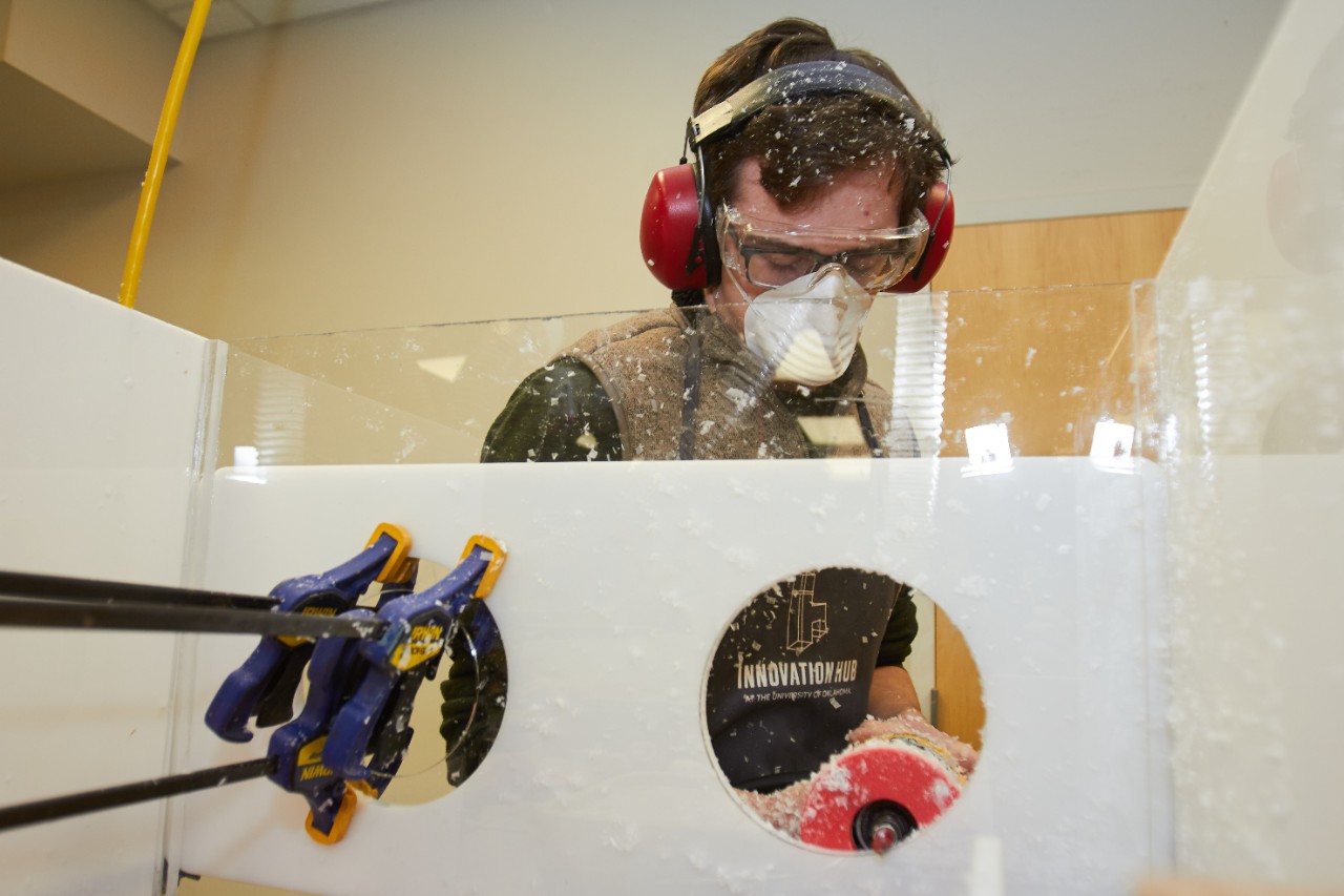 Nathan Herring, a tech lead with the Tom Love Innovation Hub, uses a palm router and pattern bit to build a prototype of an isolation box used to protect medical personnel caring for COVID-19 patients.