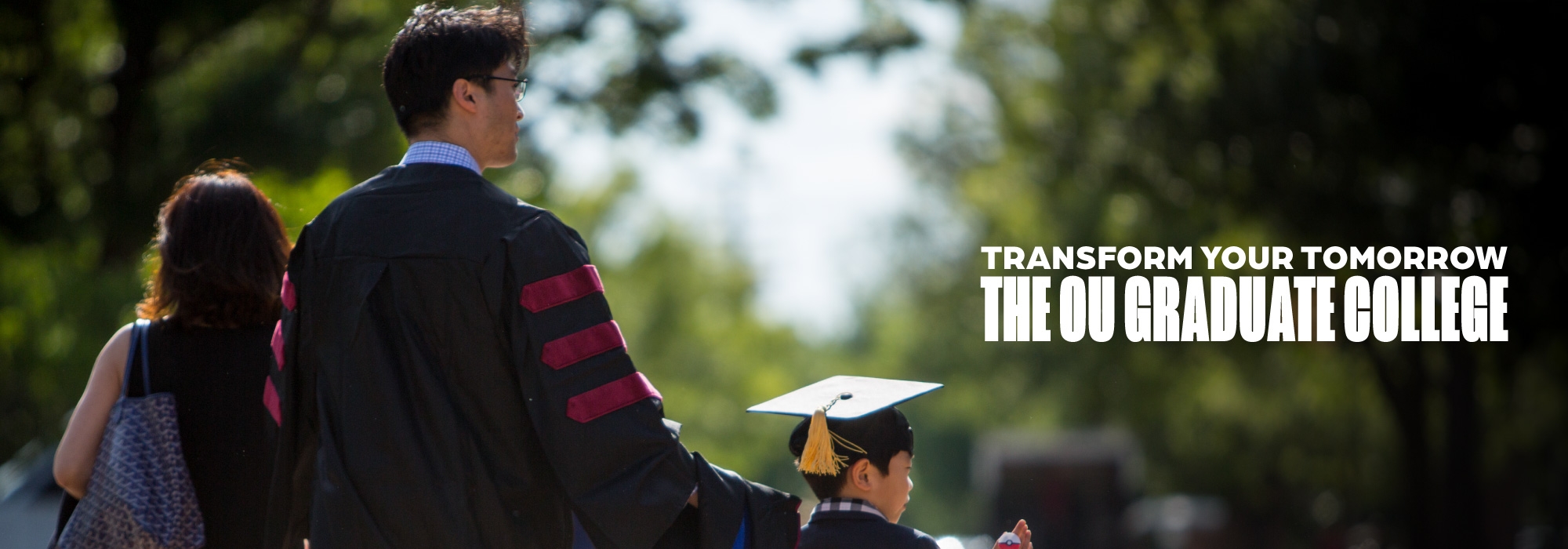 A person in graduation regalia holding the hand of a child, walking down the sidewalk.