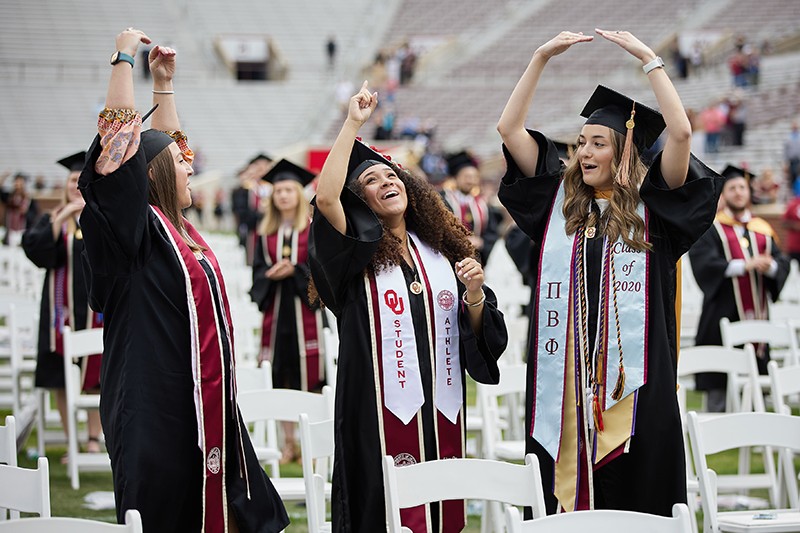 Three students in regalia celebrate from the football field