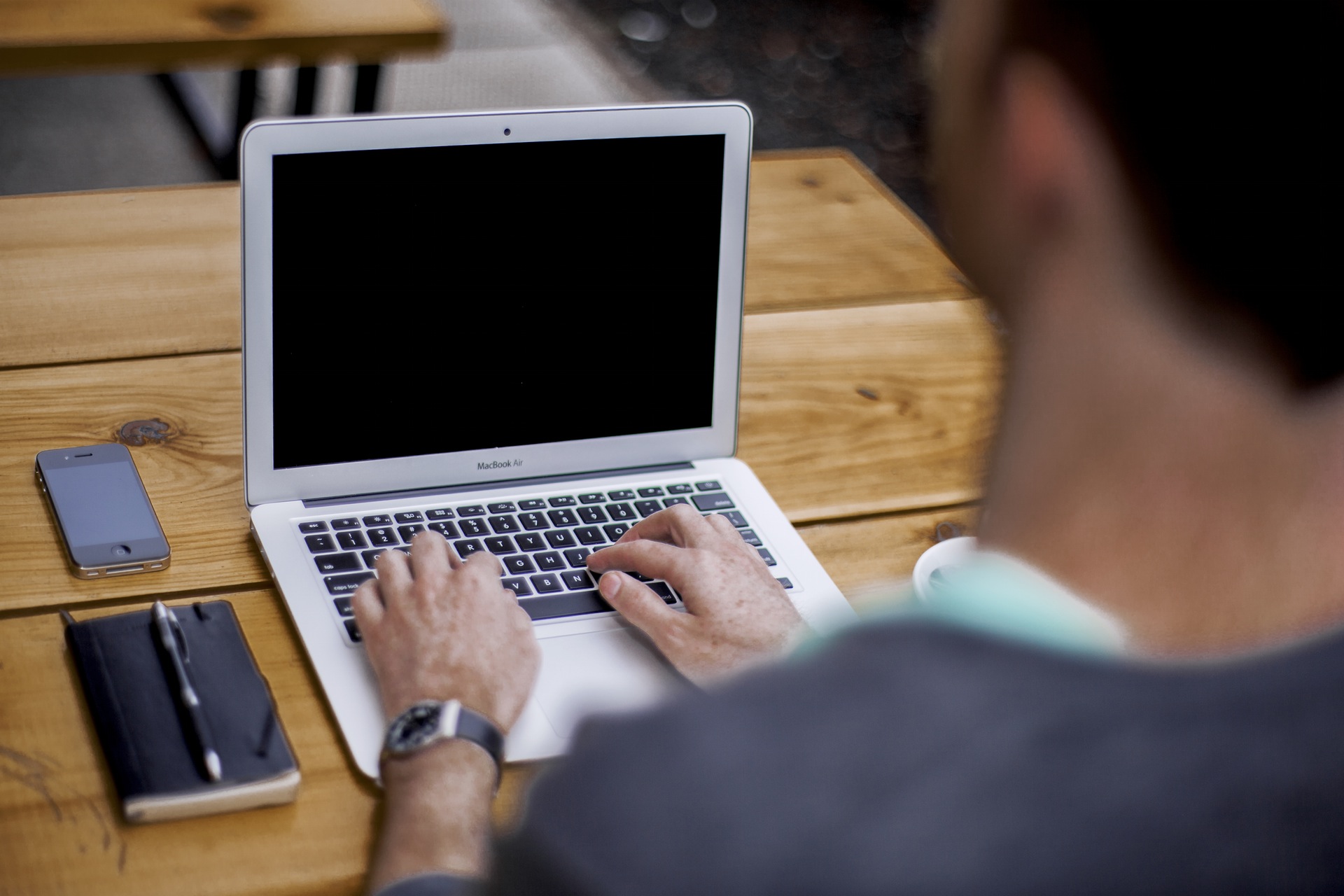 Person-typing-on-a-laptop-with-phone-and-notebook-next-to-them