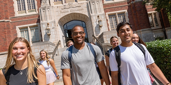 A varied group of students, male and female walk down the main staircase of Price Hall