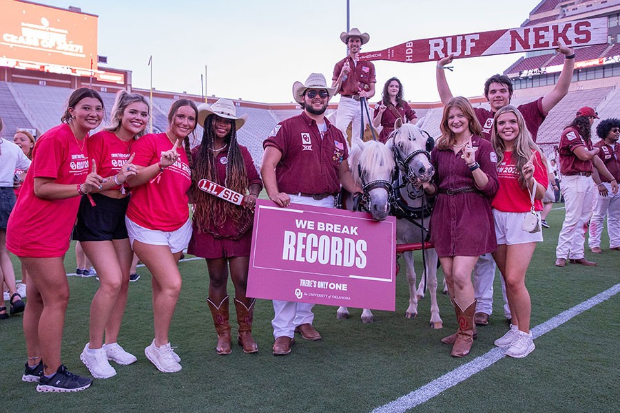 A large group of incoming freshman stand on the OU Memorial Football Field dressed in OU branded t-shirts celebrating the beginning of the new semester. 