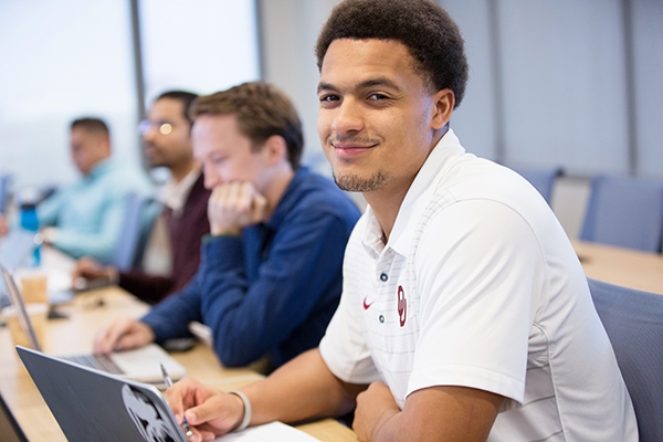 Graduate students sitting in a classroom listening and taking notes on laptops