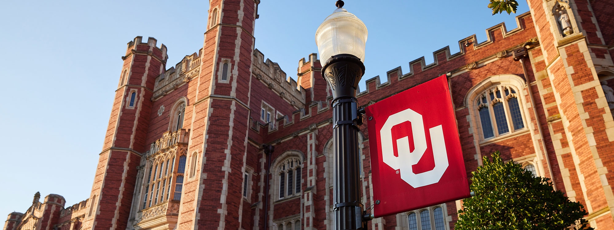 OU flag on light pole in front of Evans Hall, a large brick building.