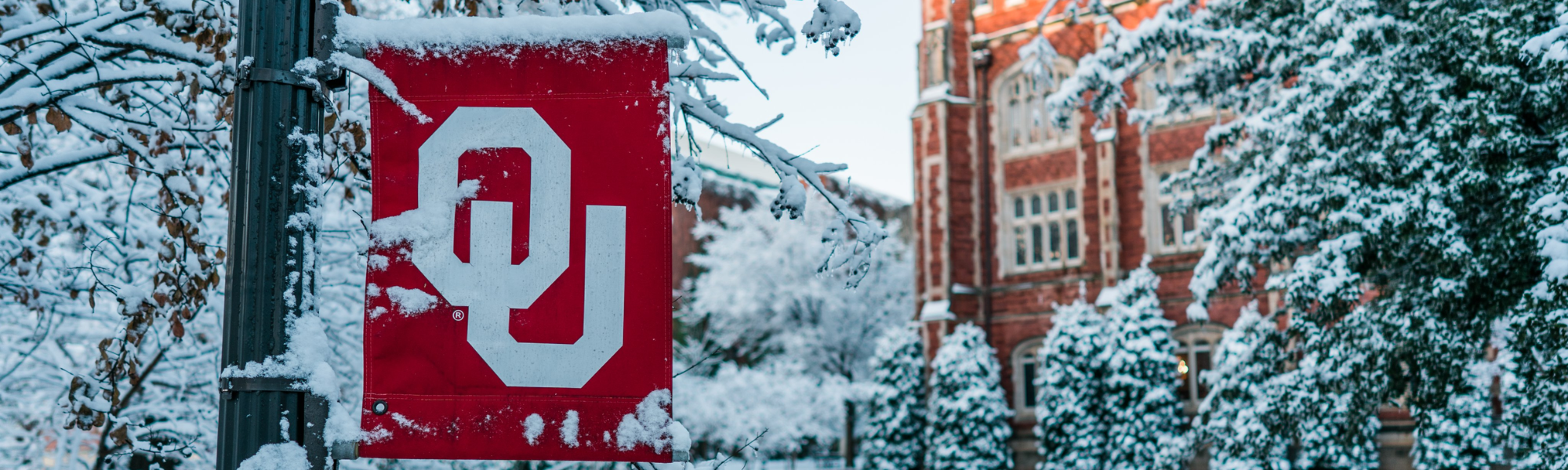 An OU banner and a campus building dusted in snow.