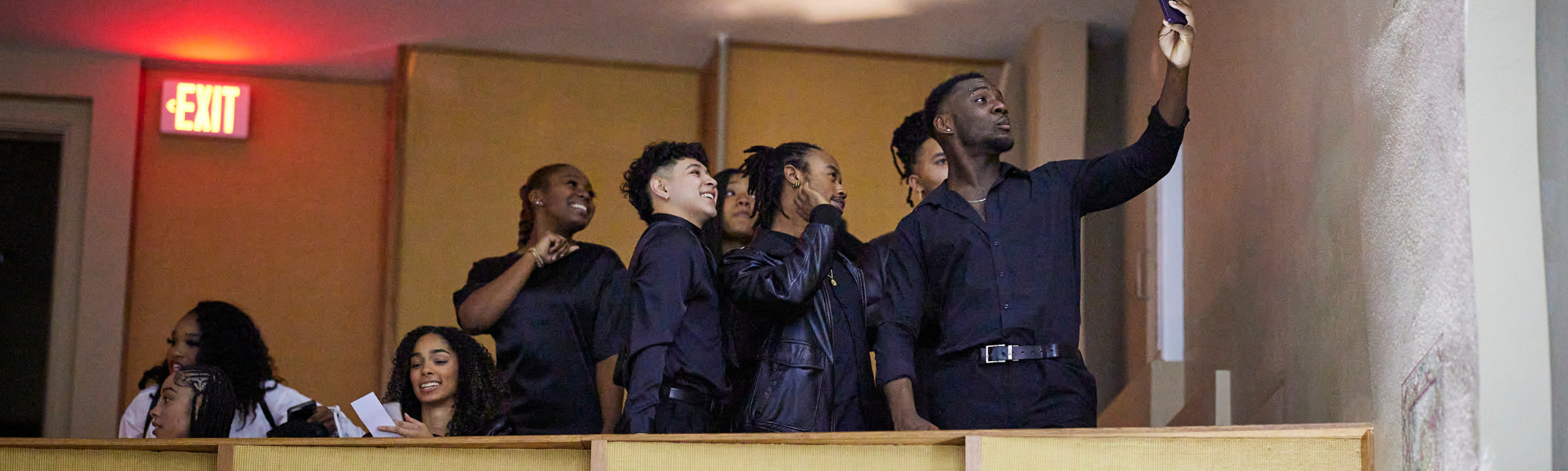 A group of students taking a selfie in the balcony of an auditorium at an event.