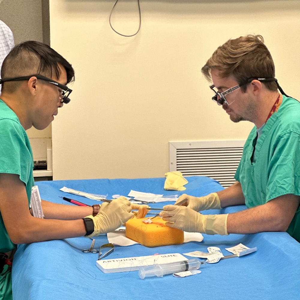 Two students practicing medical techniques with a kit.