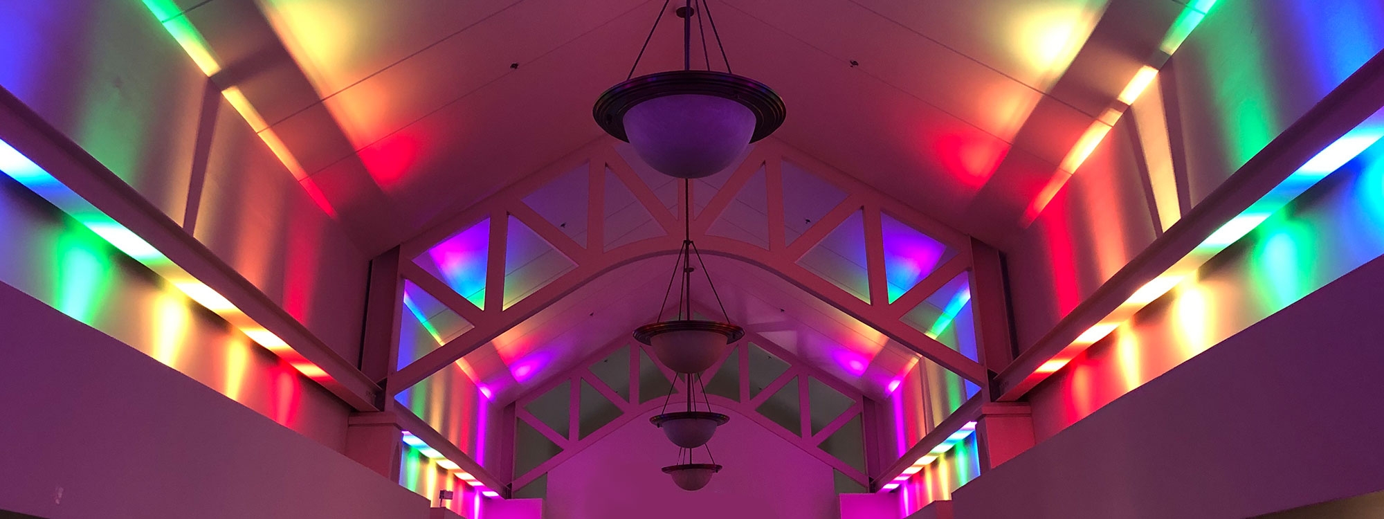 A multi-colored lighting shining up walls in large open-space room.